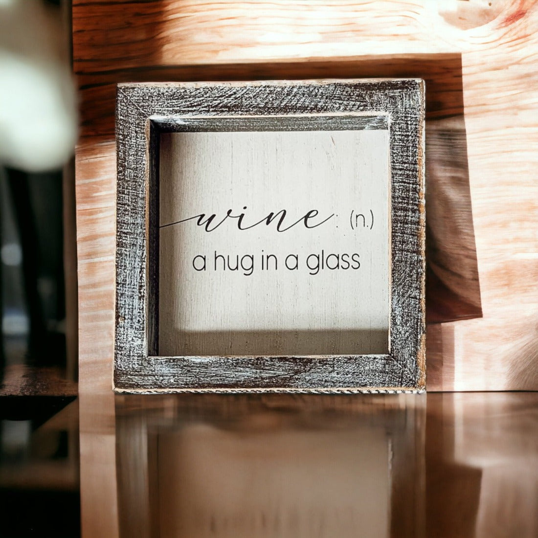 A beautifully framed wooden sign that reads 'Wine: A Hug', featuring a white-washed finish, perfect for home decor.