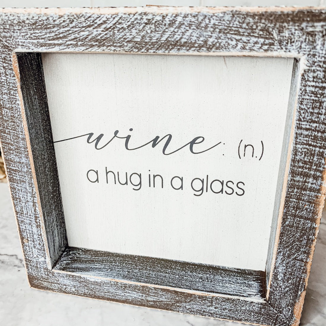 A beautifully framed wooden sign that reads 'Wine: A Hug', featuring a white-washed finish, perfect for home decor.