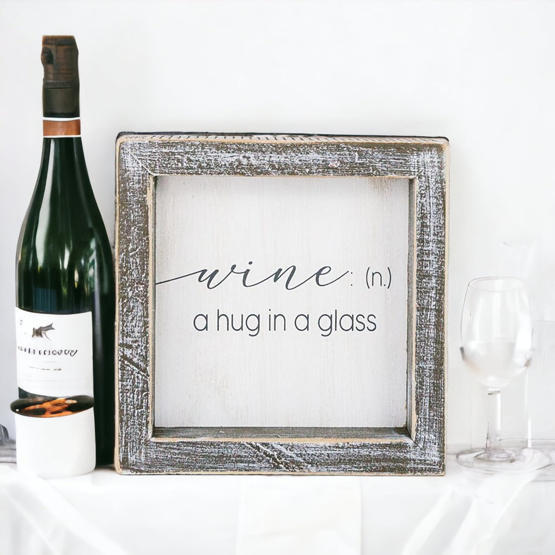 A beautifully framed wooden sign that reads 'Wine: A Hug', featuring a white-washed finish, perfect for home decor.