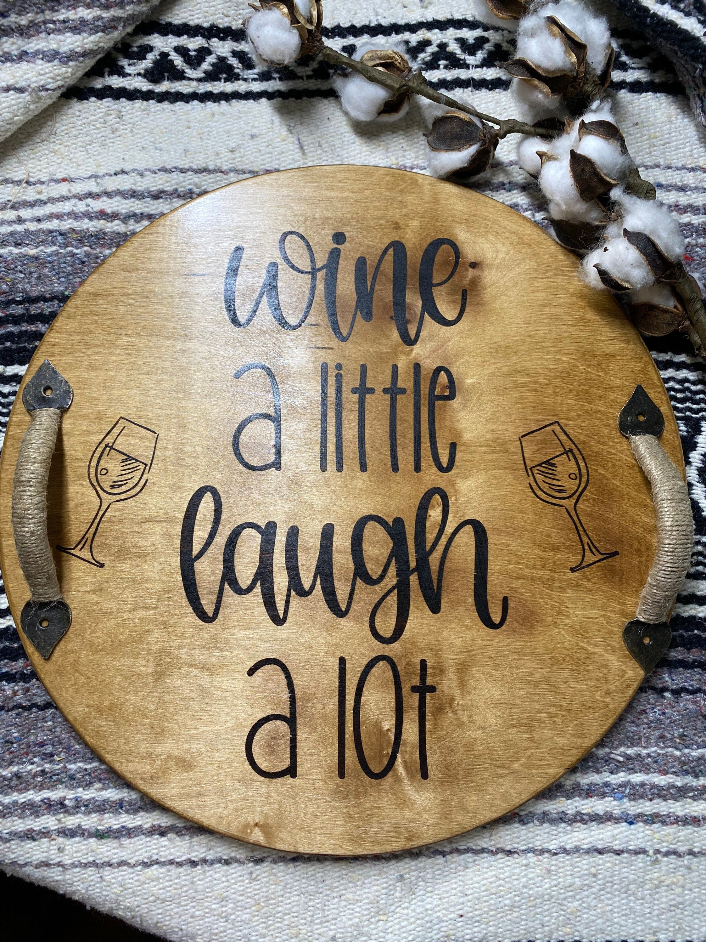 Rustic round wooden serving tray with twine wrapped metal handles and a burned sentiment, perfect for wine serving.