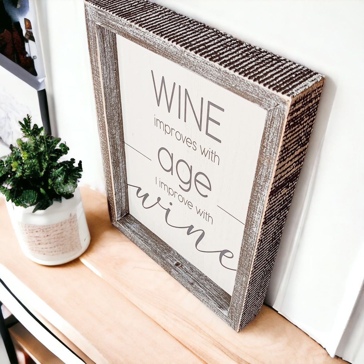 A stylish wood sign that reads 'Wine improves with age, I improve with wine', featuring a modern design in white and grey colors.