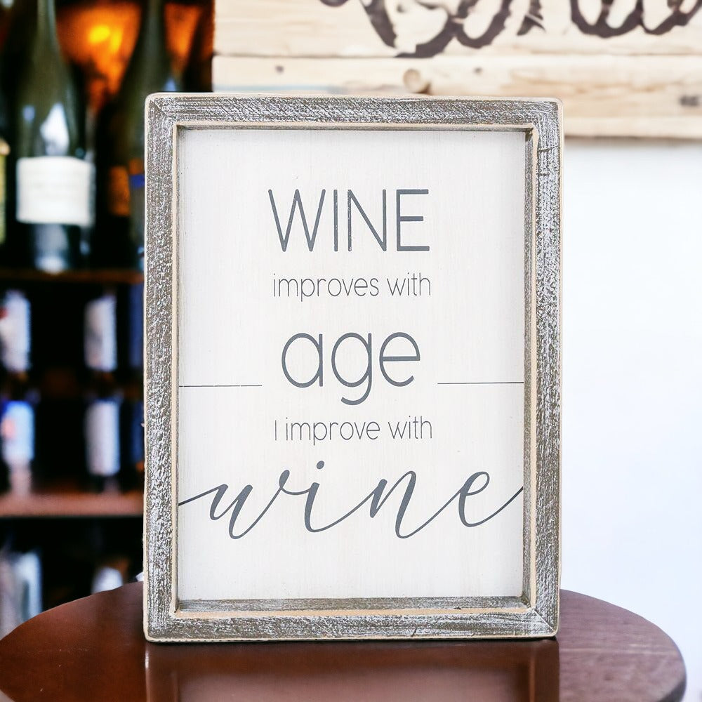 A stylish wood sign that reads 'Wine improves with age, I improve with wine', featuring a modern design in white and grey colors.