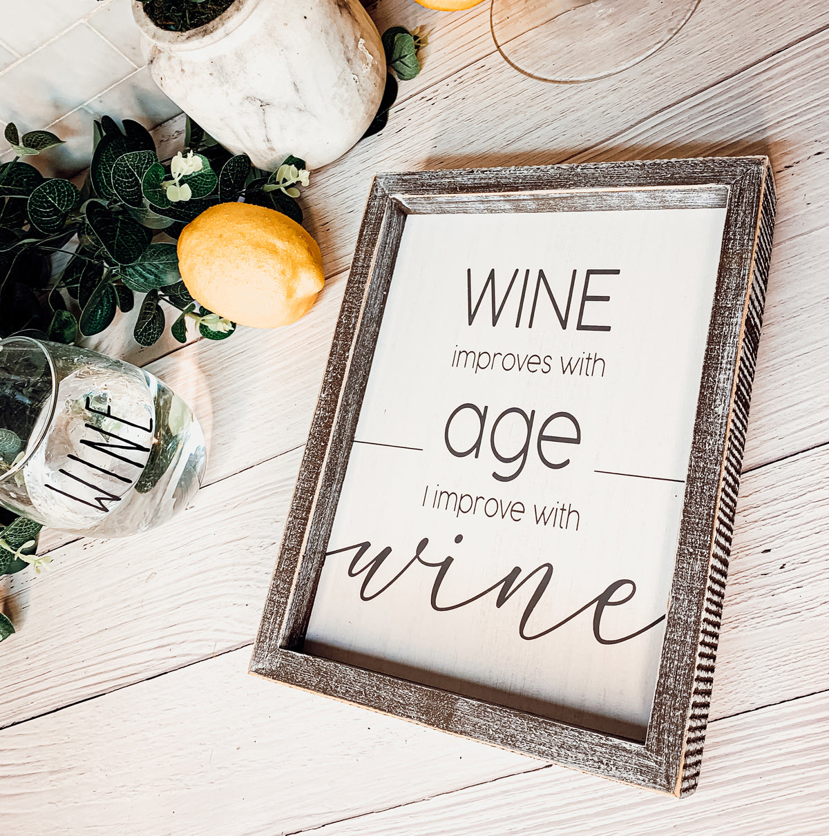 A stylish wood sign that reads 'Wine improves with age, I improve with wine', featuring a modern design in white and grey colors.