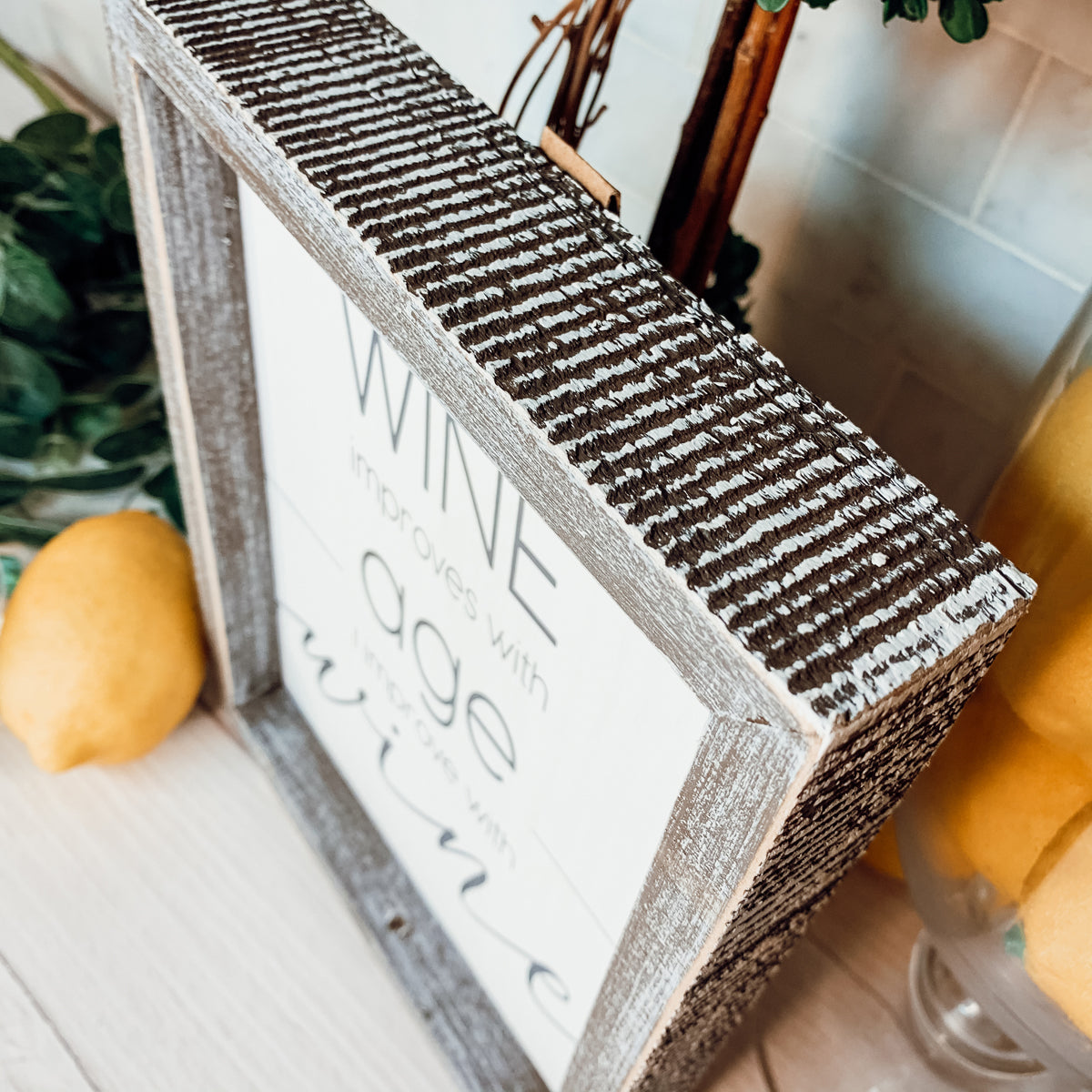 A stylish wood sign that reads 'Wine improves with age, I improve with wine', featuring a modern design in white and grey colors.