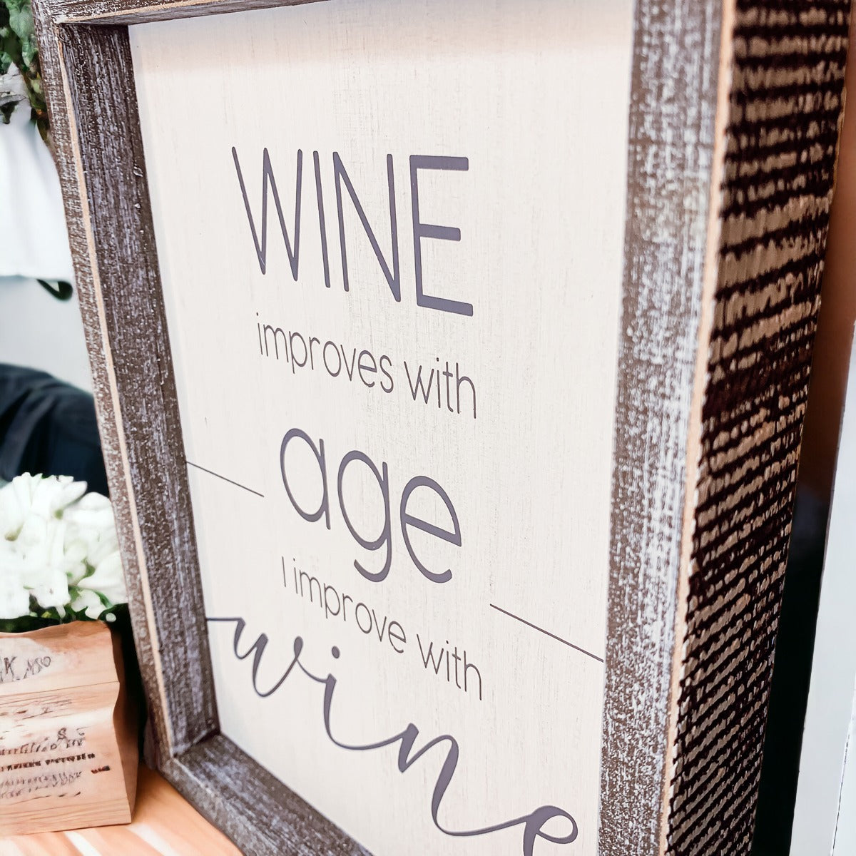 A stylish wood sign that reads 'Wine improves with age, I improve with wine', featuring a modern design in white and grey colors.