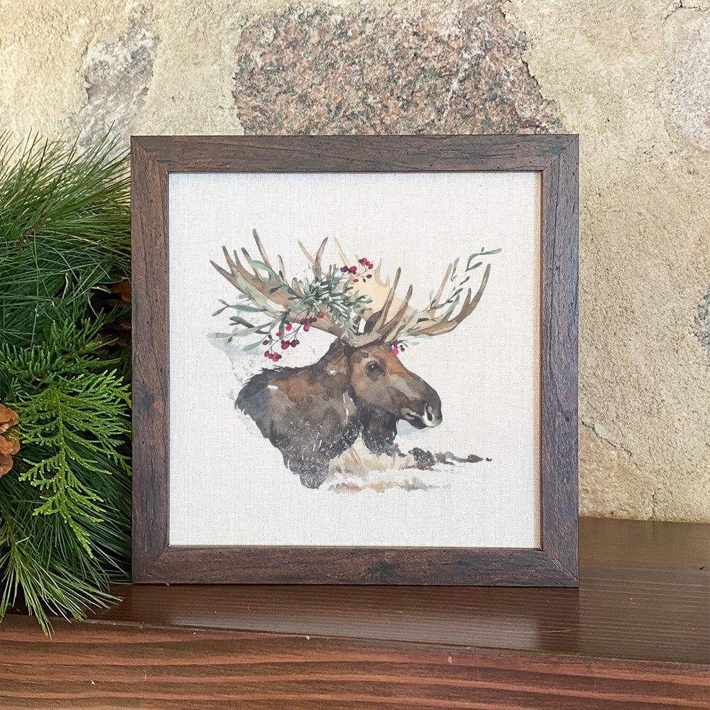 A beautifully framed sign featuring a winter moose design, set in a natural wood frame with a linen-look background.