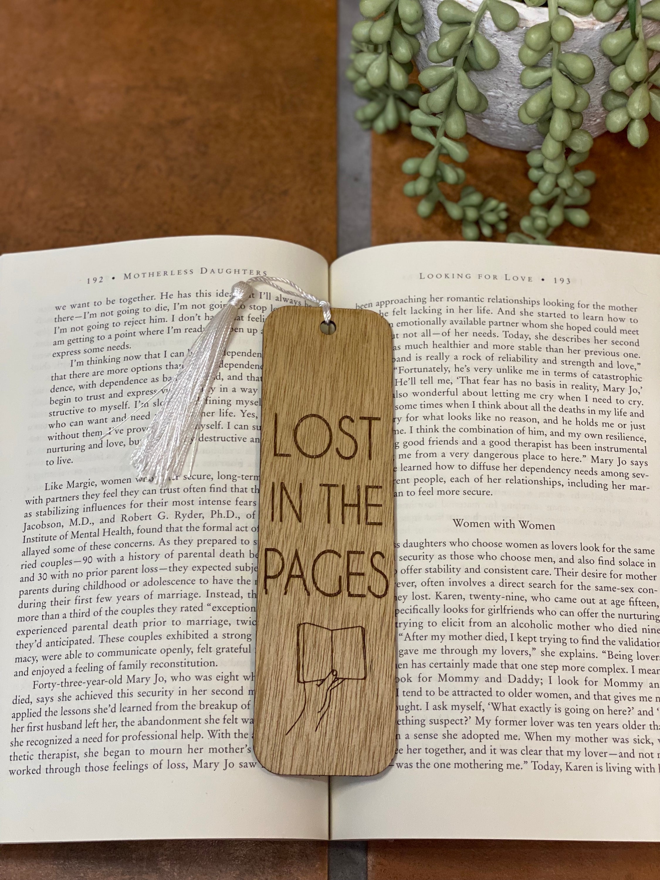 A beautifully crafted wooden bookmark with intricate laser engraving and a white tassel, resting on an open book.