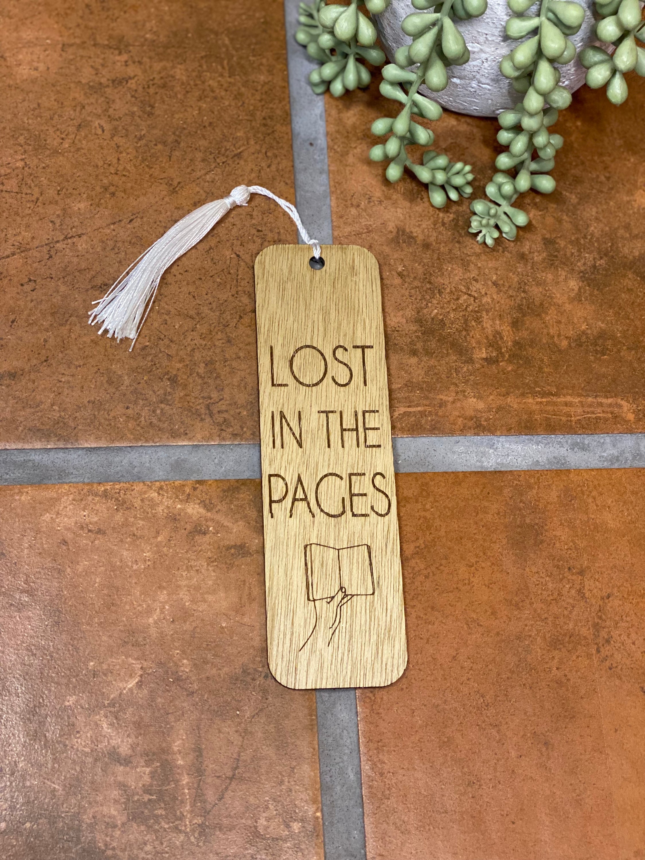 A beautifully crafted wooden bookmark with intricate laser engraving and a white tassel, resting on an open book.