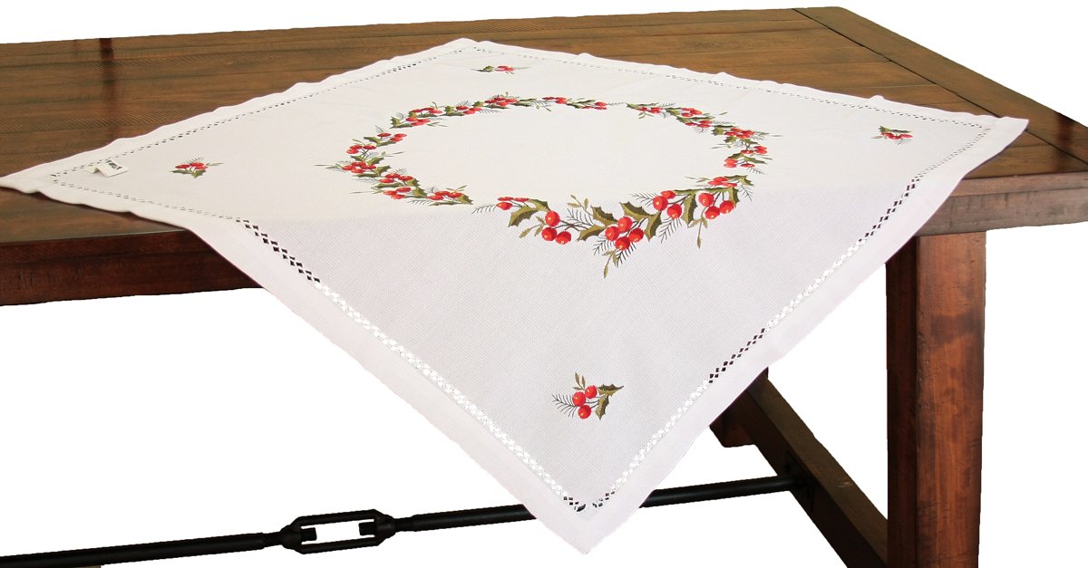 XD108059 Holly Berry Table Topper featuring intricate embroidery of holly leaves and berries, elegantly hemstitched, perfect for Christmas decor.