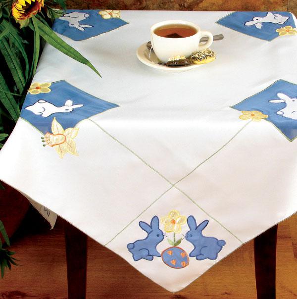 XD67703 Baby Bunnies Table Topper featuring blue bunnies, flowers, and Easter eggs with green stitch trim, perfect for Easter decor.