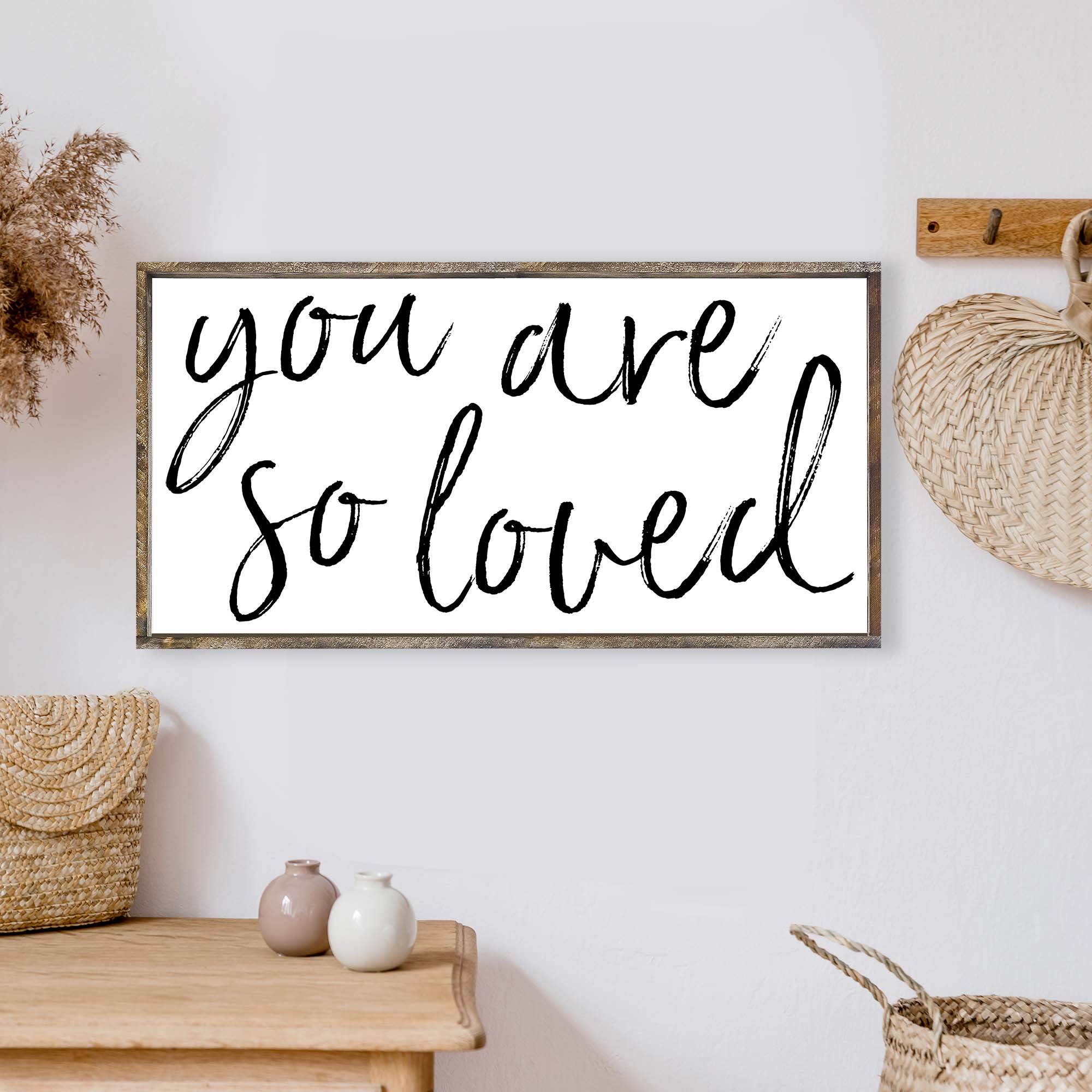 A beautifully crafted 'You Are So Loved' wood sign, measuring 25x13 inches, featuring a rustic wood stain frame and waterproof black text on a white background.