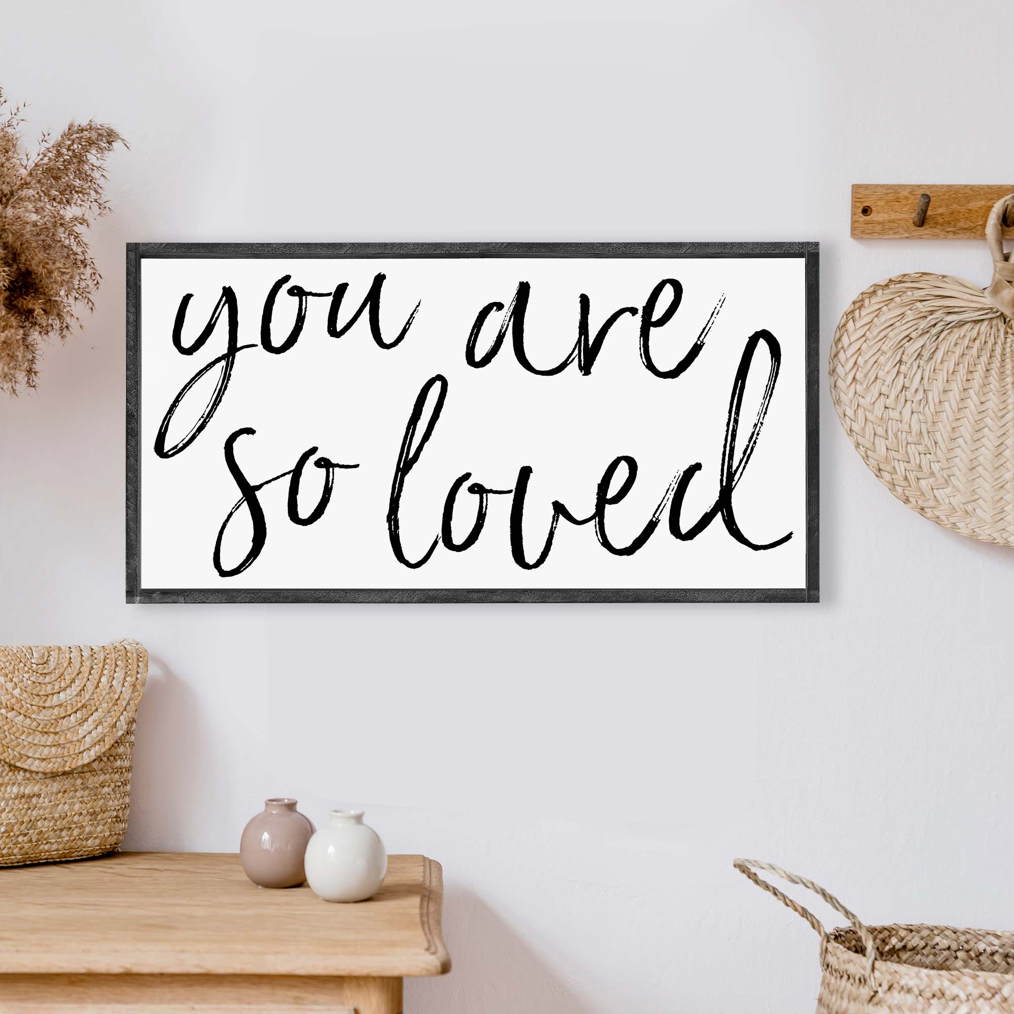 A beautifully crafted 'You Are So Loved' wood sign, measuring 25x13 inches, featuring a rustic wood stain frame and waterproof black text on a white background.