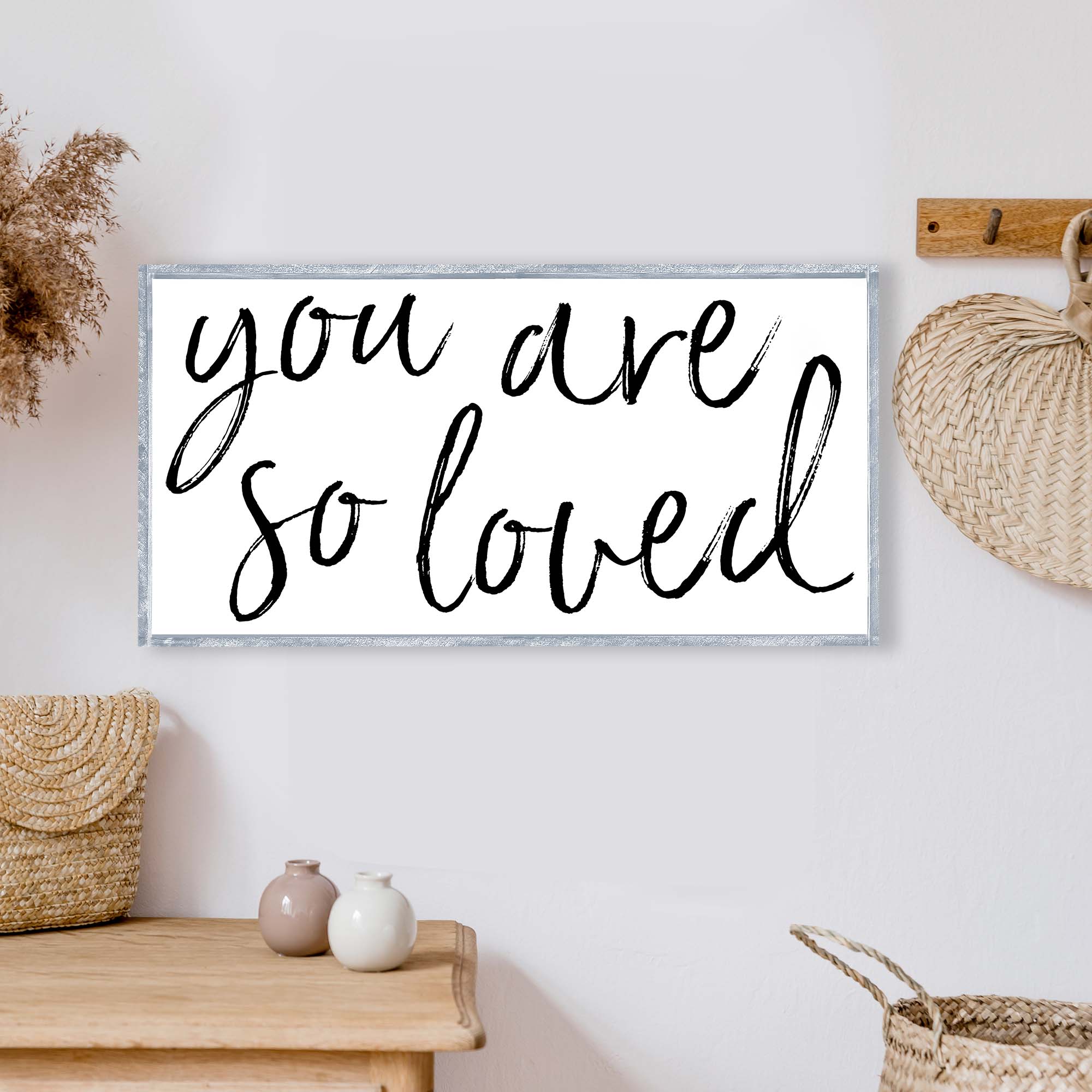 A beautifully crafted 'You Are So Loved' wood sign, measuring 25x13 inches, featuring a rustic wood stain frame and waterproof black text on a white background.