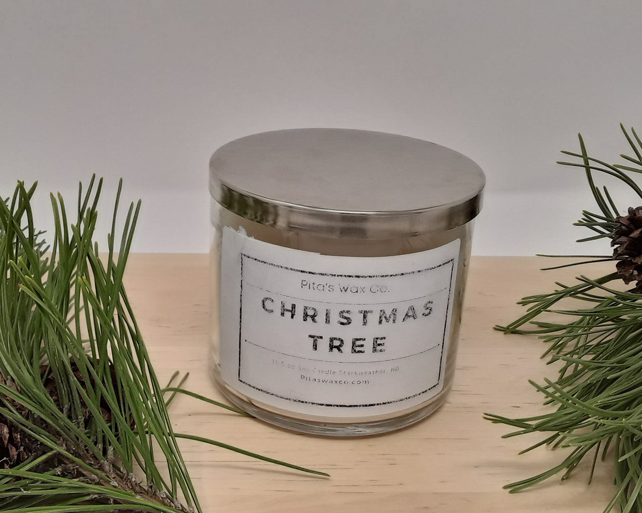 A beautifully crafted Christmas tree scented candle in a clear glass jar with a silver hammered lid, showcasing its three wicks and festive design.