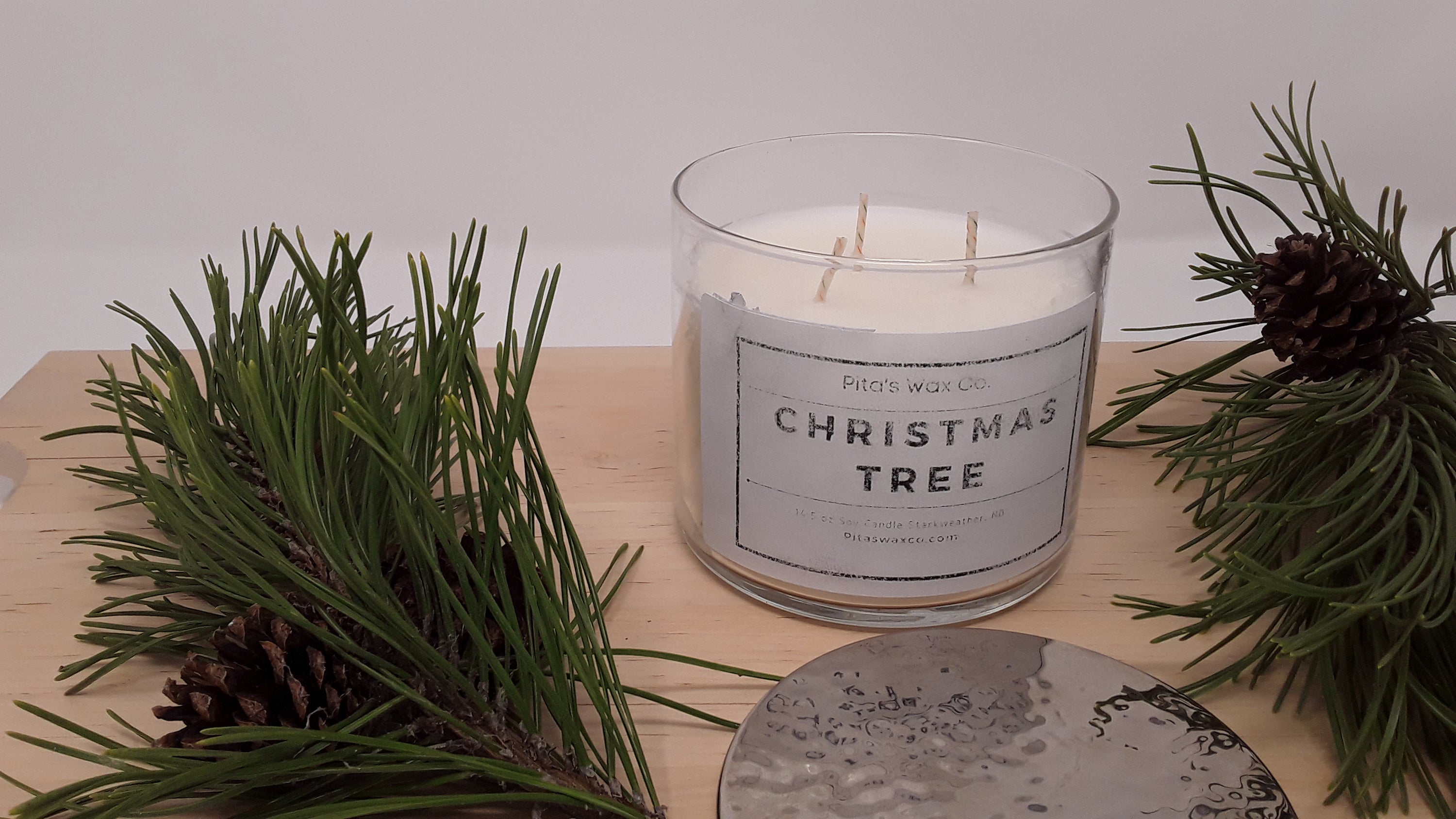 A beautifully crafted Christmas tree scented candle in a clear glass jar with a silver hammered lid, showcasing its three wicks and festive design.