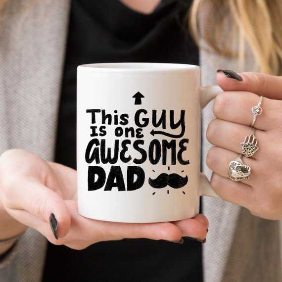 A humorous 11oz coffee mug with the text 'This Guy Is One Awesome Dad' printed on it, showcasing a fun design perfect for gifting.