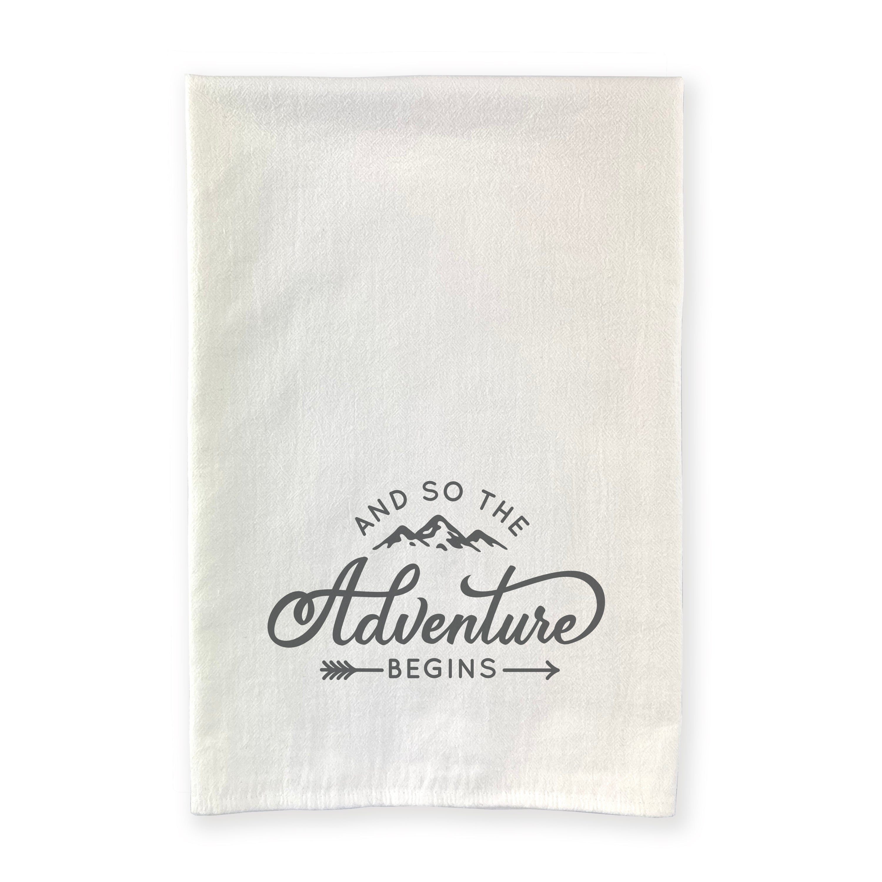 A beautifully designed cotton tea towel featuring the phrase 'And so the Adventure Begins', showcasing vibrant colors and hemmed edges.