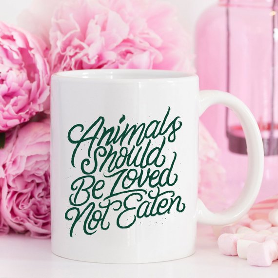 A humorous ceramic coffee mug with the phrase 'Animals Should Be Loved, Not Eaten' printed on it, showcasing a fun design for animal lovers.