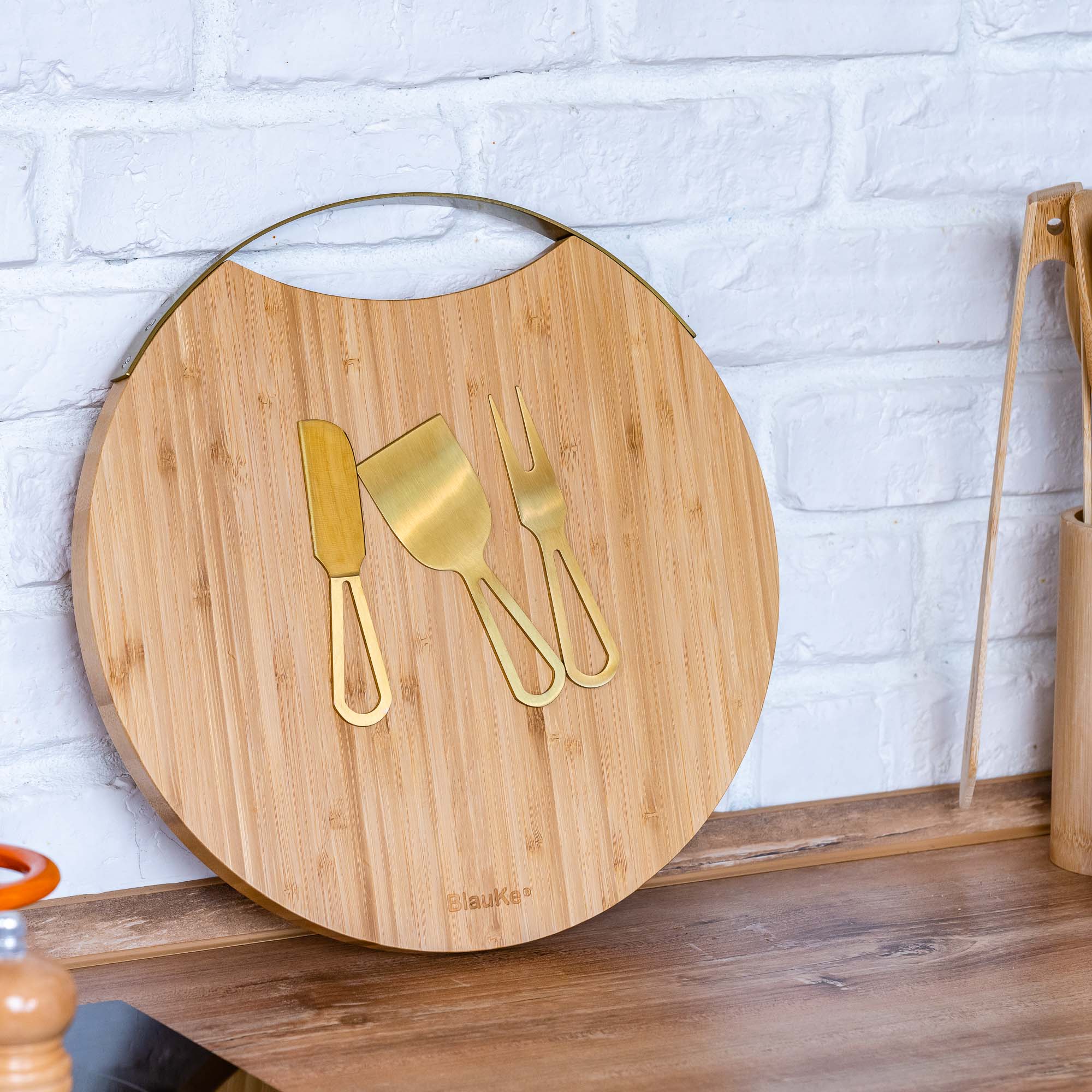 A stylish 13-inch bamboo cheese board with magnetic knife storage, featuring a spatula knife, plane knife, and serving fork, elegantly arranged for serving.