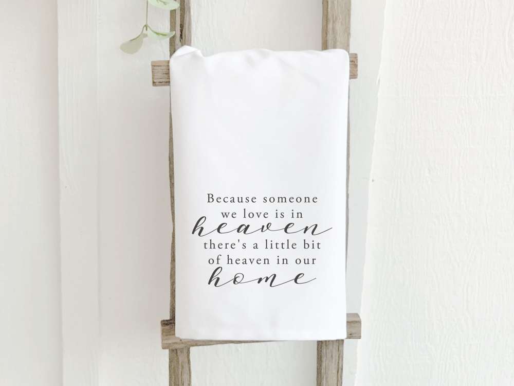 A beautiful cotton tea towel featuring the phrase 'Because Someone We Love is in Heaven', designed with vibrant colors and hemmed edges.