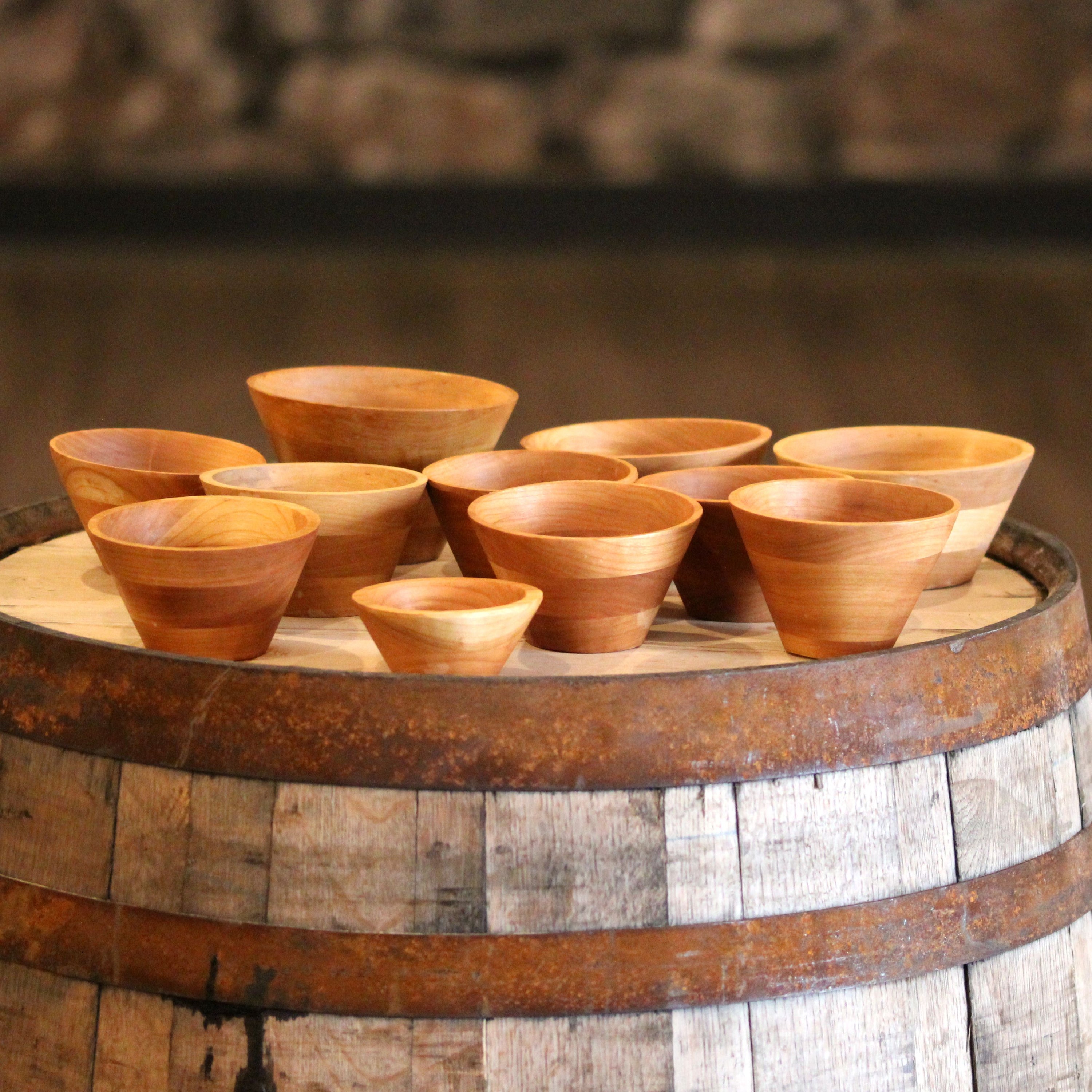 A collection of hand-turned wooden bowls in various sizes, showcasing their modern cone shape and natural wood grain.