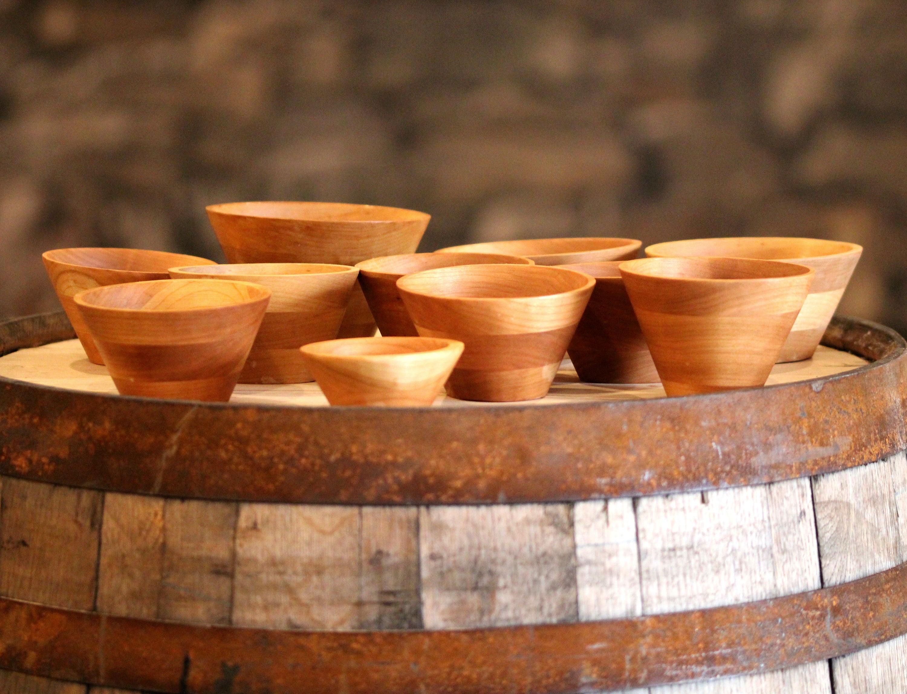 A collection of hand-turned wooden bowls in various sizes, showcasing their modern cone shape and natural wood grain.