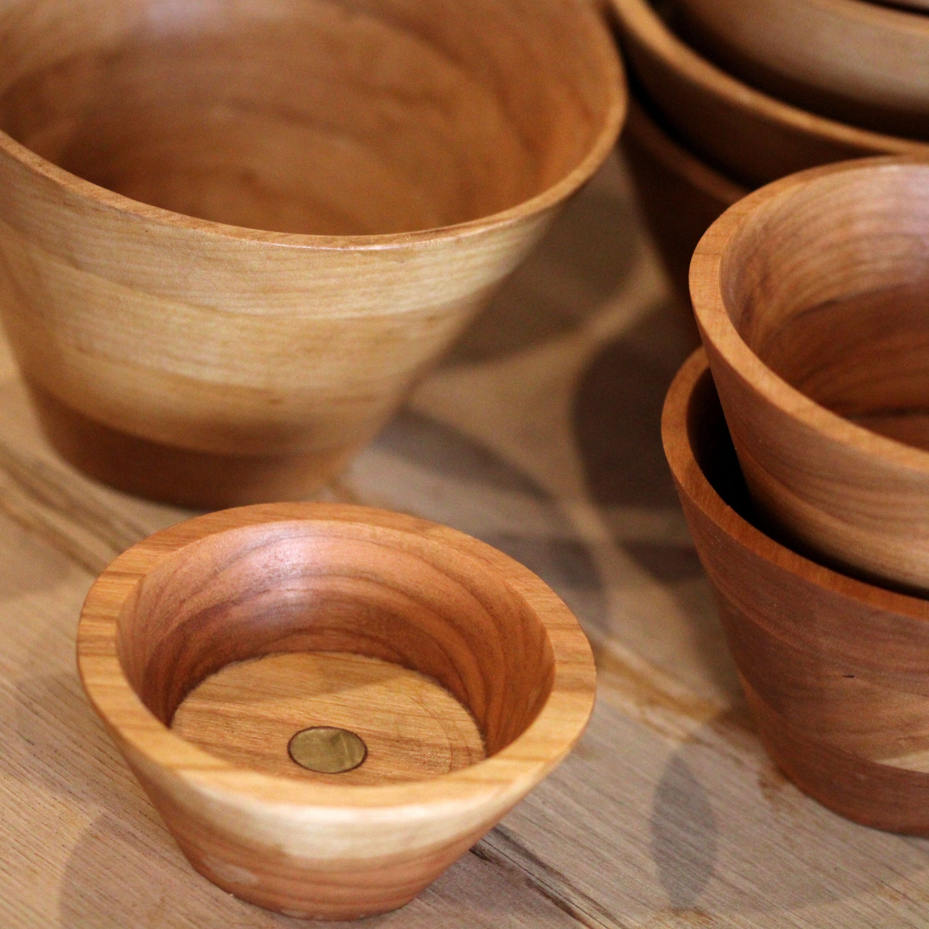 A collection of hand-turned wooden bowls in various sizes, showcasing their modern cone shape and natural wood grain.