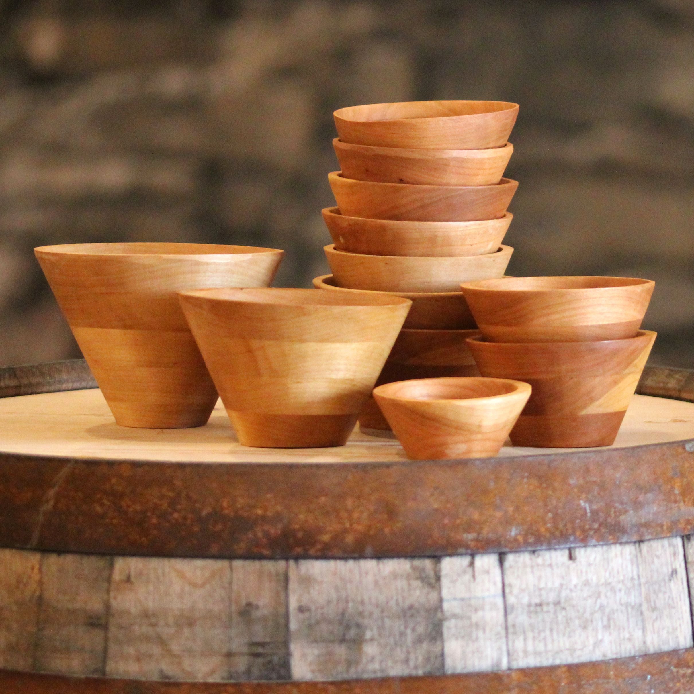 A collection of hand-turned wooden bowls in various sizes, showcasing their modern cone shape and natural wood grain.