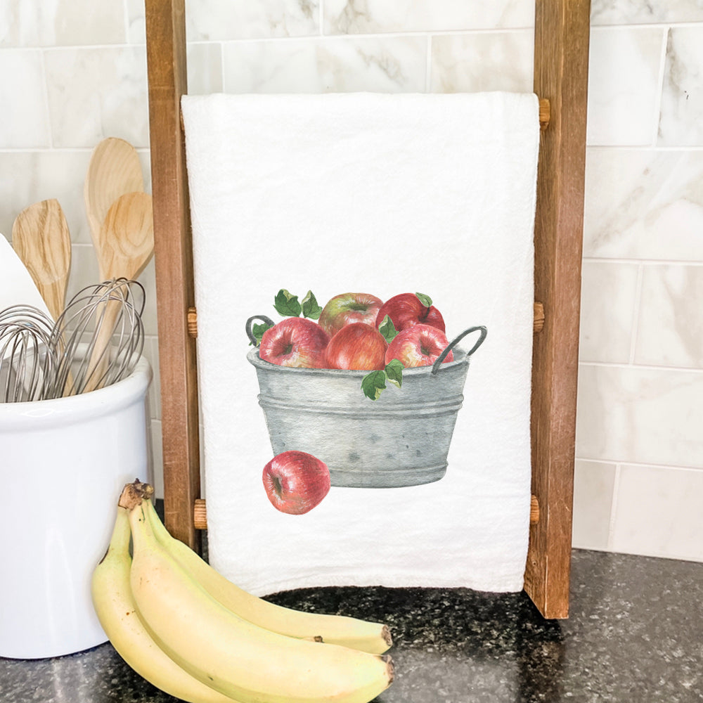 A vibrant cotton tea towel featuring a bucket of red apples design, perfect for kitchen use.