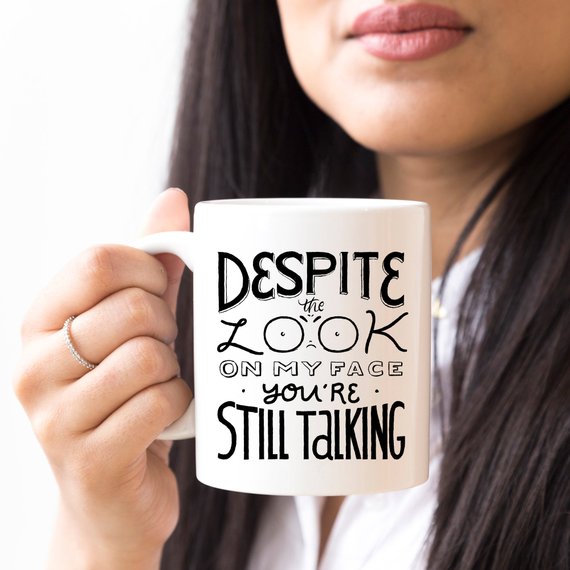 A humorous coffee mug featuring the phrase 'Despite The Look On My Face, You're Still Talking', crafted from high-quality ceramic with a glossy finish.