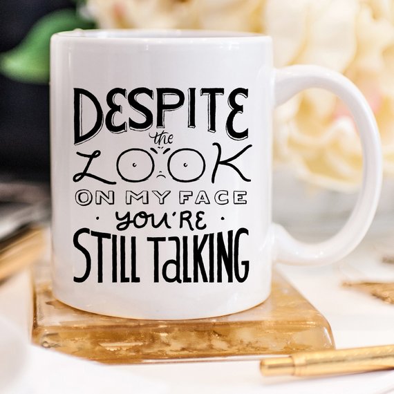 A humorous coffee mug featuring the phrase 'Despite The Look On My Face, You're Still Talking', crafted from high-quality ceramic with a glossy finish.