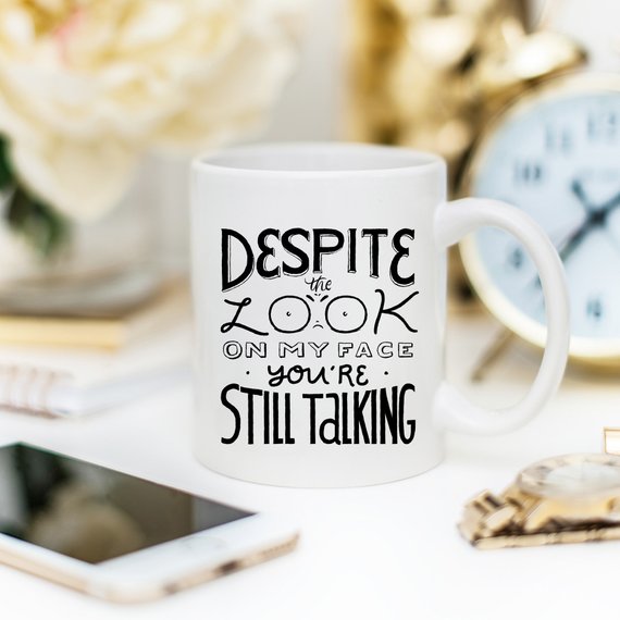 A humorous coffee mug featuring the phrase 'Despite The Look On My Face, You're Still Talking', crafted from high-quality ceramic with a glossy finish.