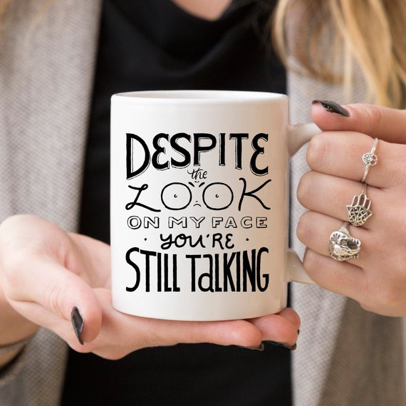 A humorous coffee mug featuring the phrase 'Despite The Look On My Face, You're Still Talking', crafted from high-quality ceramic with a glossy finish.