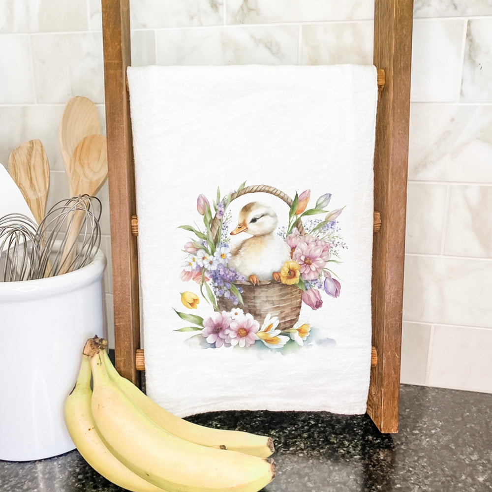 A charming cotton tea towel featuring a duckling in a flower basket design, showcasing vibrant colors and hemmed edges.