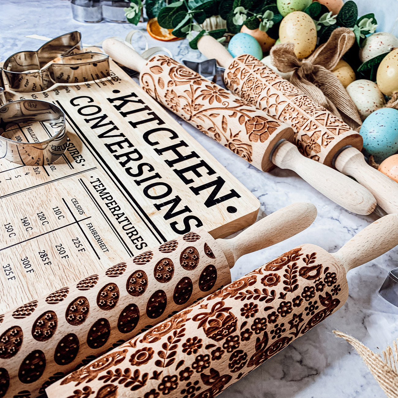 Colorful Easter and Spring rolling pins with floral and bunny designs, accompanied by two metal cookie cutters, perfect for festive baking.