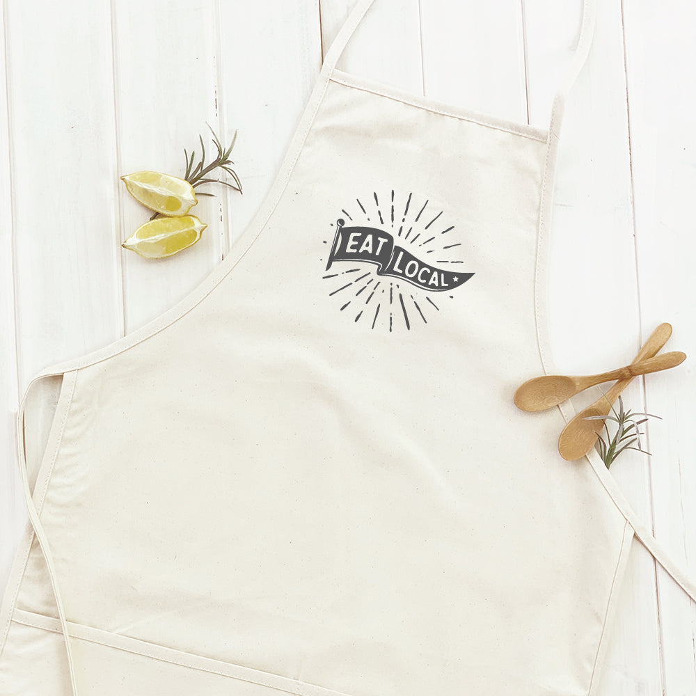 Eat Local Women's Apron made from durable cotton canvas with natural twill ties and a divided front pocket, featuring eco-friendly printed design.