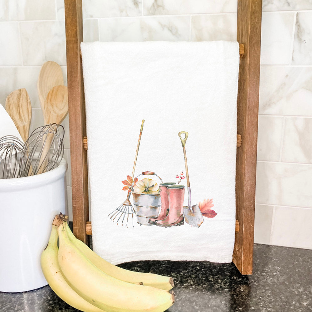 A beautifully designed cotton tea towel featuring fall boots and garden tools, showcasing vibrant colors and hemmed edges.