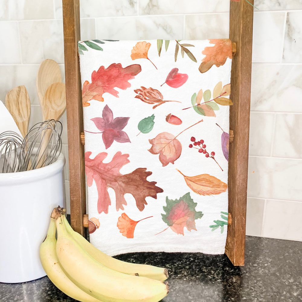 A vibrant cotton tea towel featuring a fall leaves pattern, showcasing rich autumn colors and hemmed edges, perfect for kitchen use.