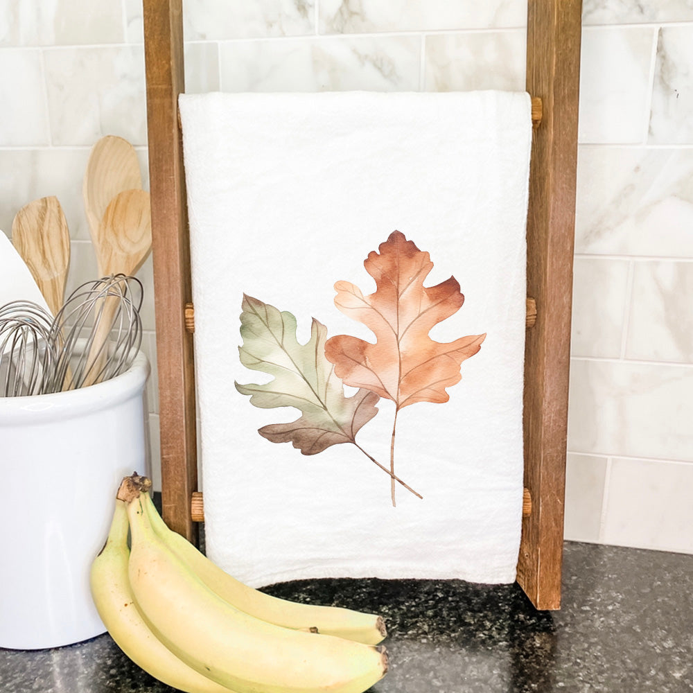 A vibrant cotton tea towel featuring a beautiful fall oak leaves design, perfect for kitchen use.