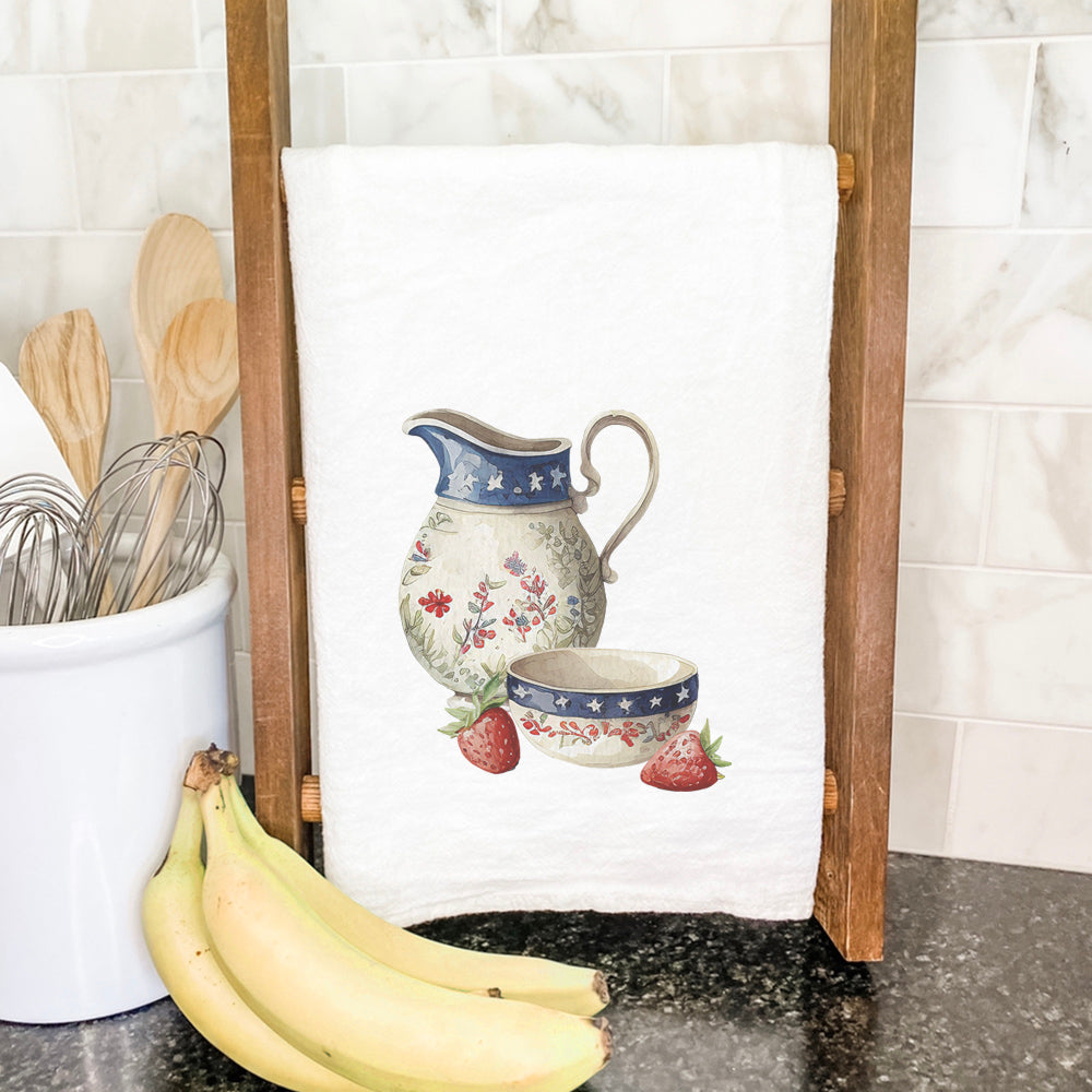 A beautifully designed cotton tea towel featuring a farmhouse pitcher and bowl, showcasing vibrant colors and hemmed edges.