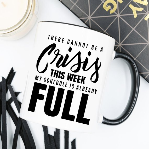 A humorous coffee mug with the phrase 'There Cannot Be A Crisis This Week' printed on it, showcasing a fun design perfect for office gifts.