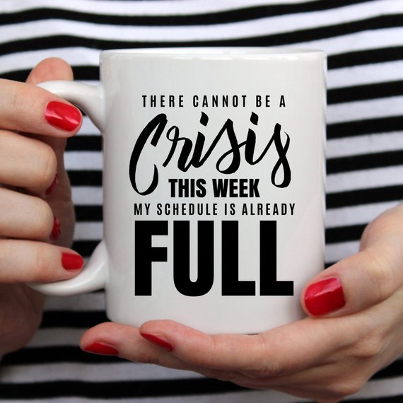 A humorous coffee mug with the phrase 'There Cannot Be A Crisis This Week' printed on it, showcasing a fun design perfect for office gifts.