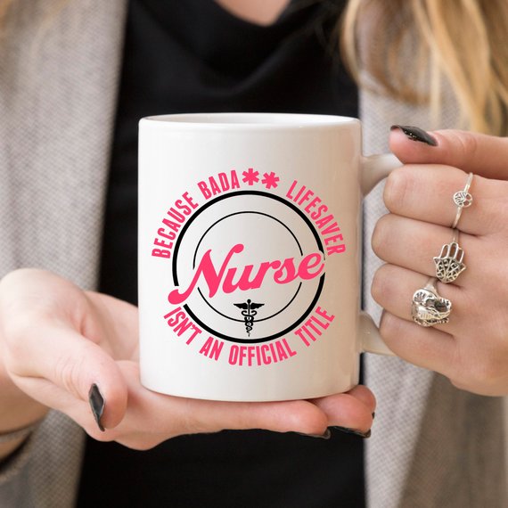 A high-quality white coffee mug featuring the text 'Nurse - Because Bada** Lifesaver Isn't An Official Title' in bold, vivid letters, perfect for nurses.