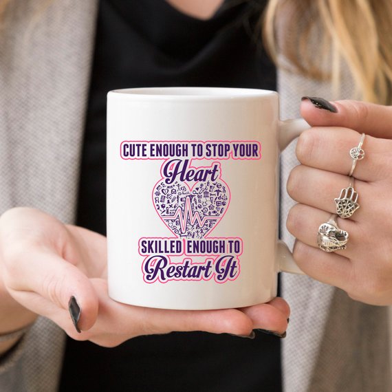 A humorous coffee mug for nurses featuring the phrase 'Cute Enough To Stop Your Heart, Skilled Enough To Restart It' with a vibrant design.