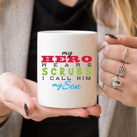 Funny Nurse Mug featuring the text 'My Hero Wears Scrubs, I Call Him My Son', perfect for coffee lovers and nursing professionals.