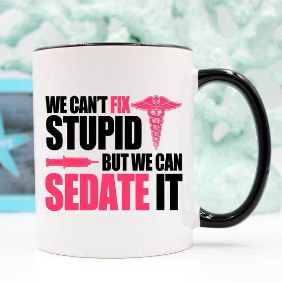 A humorous coffee mug designed for nurses, featuring the text 'We Can't Fix Stupid, But We Can Sedate It' in bold, readable font on a white ceramic background.