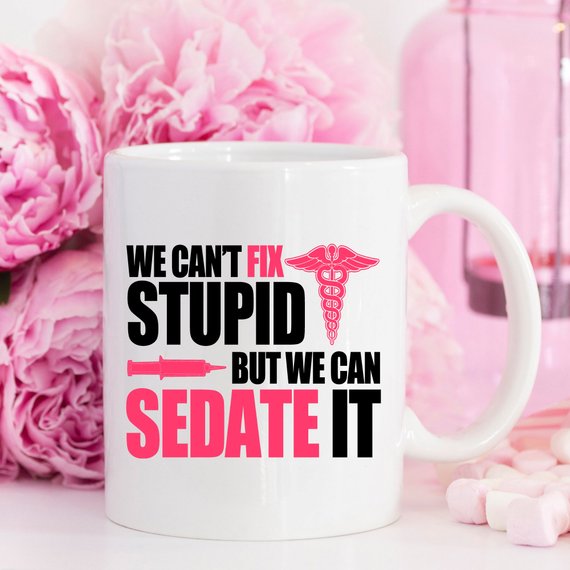 A humorous coffee mug designed for nurses, featuring the text 'We Can't Fix Stupid, But We Can Sedate It' in bold, readable font on a white ceramic background.