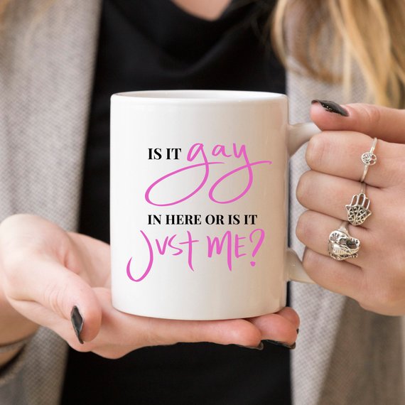 A colorful Gay Pride Mug featuring the humorous phrase 'Is It Gay In Here Or Is It Just Me?' designed for coffee lovers.