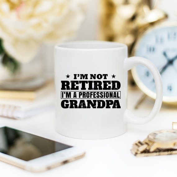 A humorous coffee mug featuring the phrase 'I'm Not Retired, I'm A Professional Grandpa', showcasing a fun design perfect for grandparents.