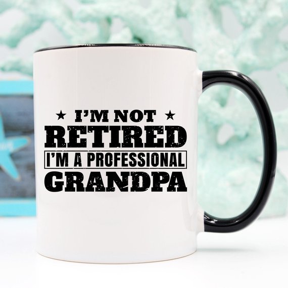 A humorous coffee mug featuring the phrase 'I'm Not Retired, I'm A Professional Grandpa', showcasing a fun design perfect for grandparents.